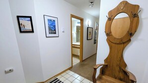 A hallway with a wooden chair, framed pictures on the walls, and a tiled floor.