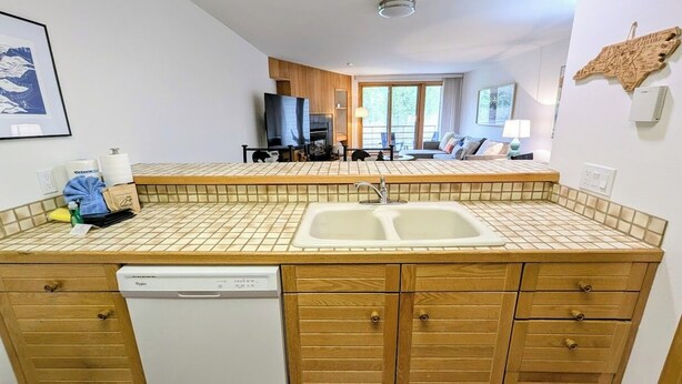 A compact kitchen with a dishwasher, wooden cabinets, and a tiled backsplash.