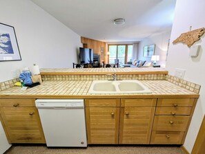 A compact kitchen with a dishwasher, wooden cabinets, and a tiled backsplash. - Ski Run 503 (Keystone)