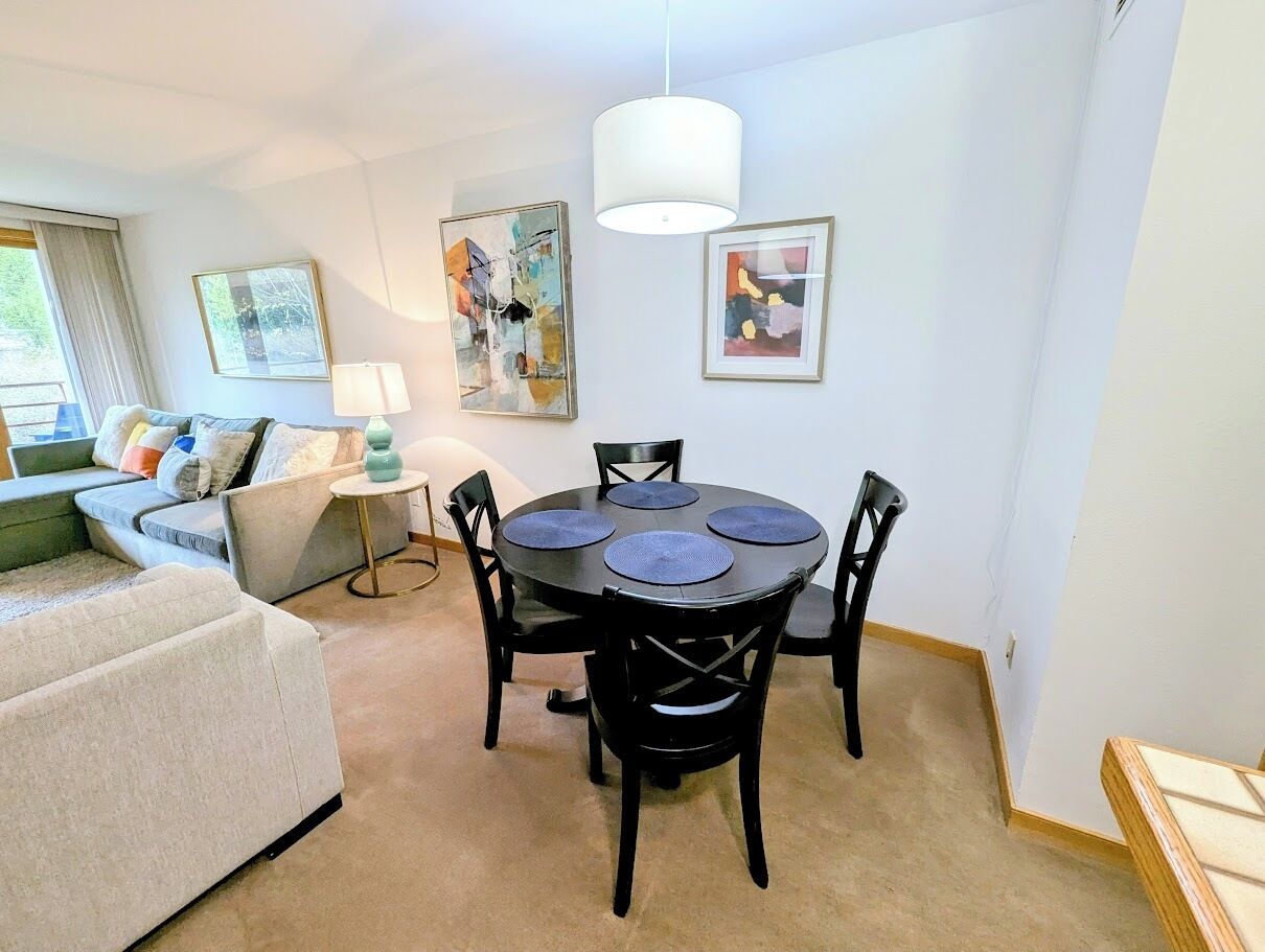 A modern living room with a round table, black chairs, a sofa, and a lamp.
