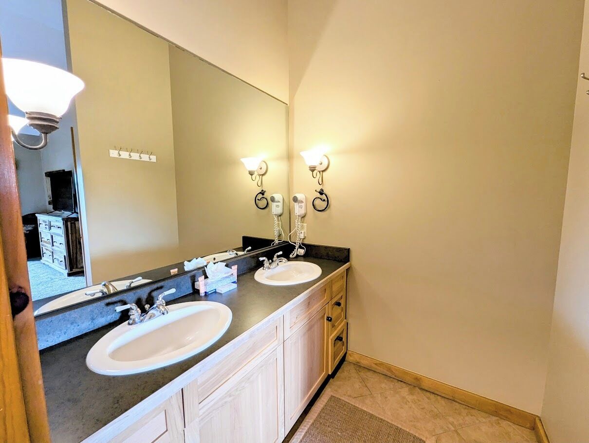 Une salle de bain avec deux lavabos, un grand miroir et des luminaires fixés au mur.