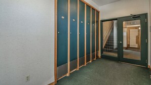 Un couloir avec une moquette verte, une porte en bois dotée d’un panneau de verre, et un escalier visible à travers le verre.