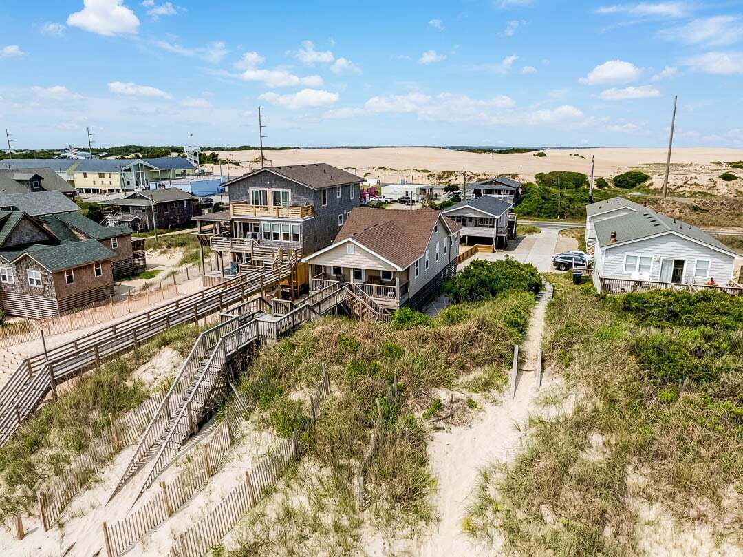 Un quartier résidentiel en bord de mer, avec des maisons, un escalier en bois et, au loin, une plage de sable.