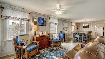 Un salon chaleureux avec un plancher en bois, un canapé en cuir marron, un fauteuil à bascule en bois, un tapis à motifs bleus et une table à manger avec des chaises.