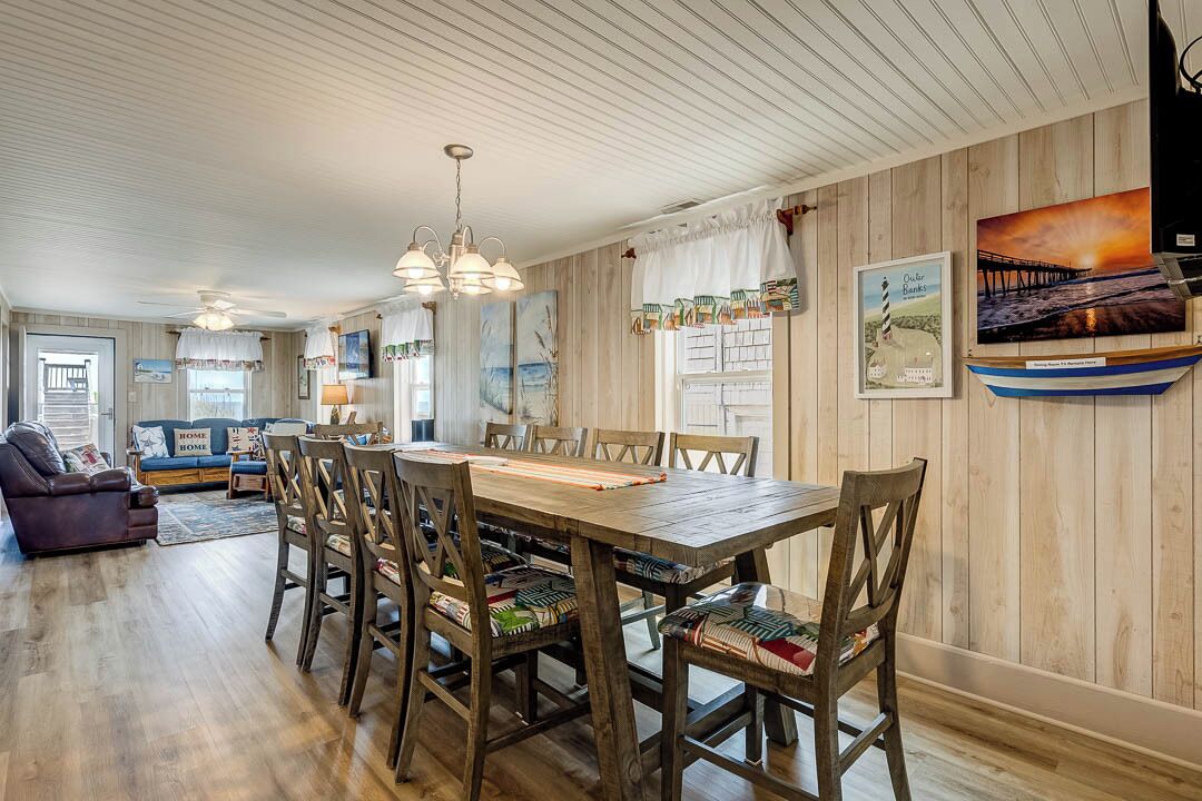 Un espace repas comprenant une table et des chaises en bois, un ventilateur de plafond et des œuvres d’art accrochées au mur.