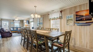 A dining area with a wooden table and chairs, a ceiling fan, and wall-mounted artwork. - Breakers | Oceanfront (Nags Head)