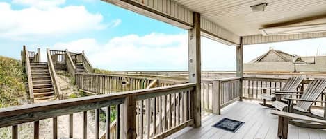 A wooden deck with a railing, a set of stairs leading to a beach, and beach chairs.