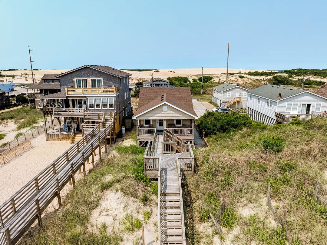 Une propriété située en bord de mer, avec une promenade en bois menant à une maison dotée d’un balcon.