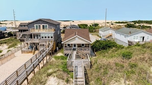A beachfront property with a wooden boardwalk leading to a house with a balcony. - Breakers | Oceanfront (Nags Head)