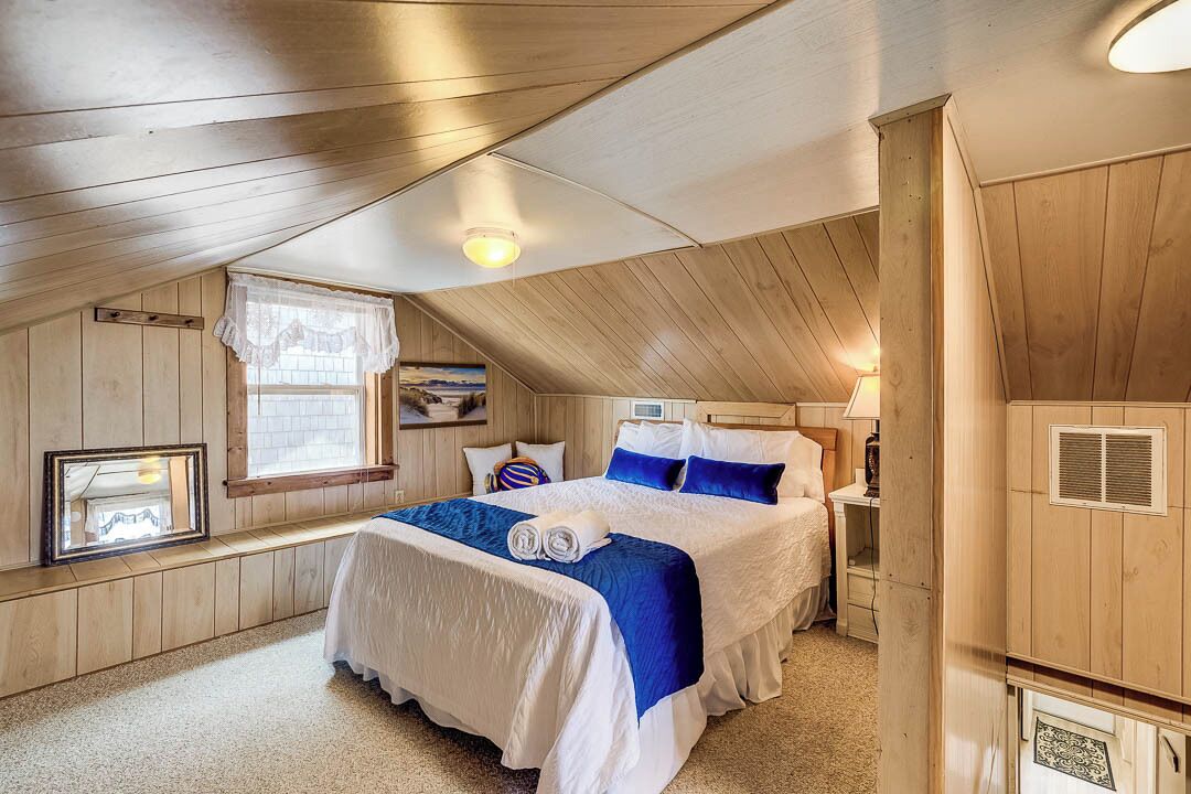 Une chambre avec un plafond en bois, un lit avec une literie bleue et blanche, une fenêtre donnant sur un beau paysage et une petite table avec une lampe.