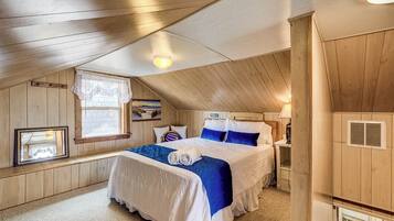 Une chambre avec un plafond en bois, un lit avec une literie bleue et blanche, une fenêtre donnant sur un beau paysage et une petite table avec une lampe.