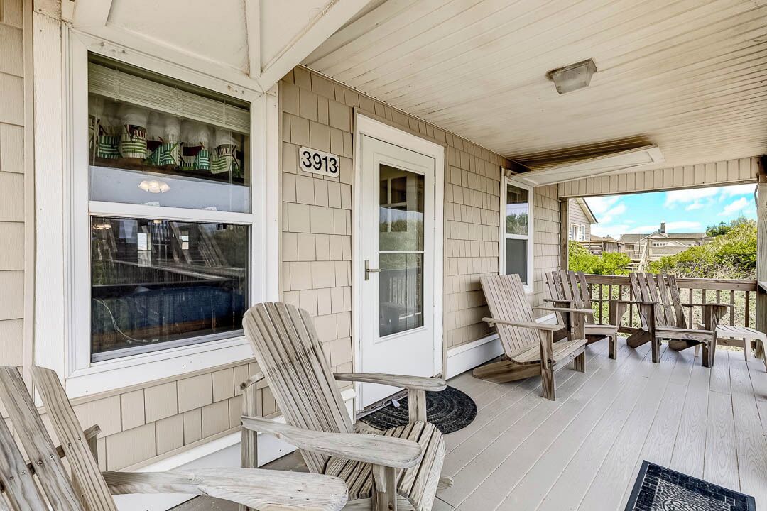 Une véranda couverte avec des chaises en bois et une table à manger, une fenêtre donnant sur le jardin, et une porte portant le numéro 3913.