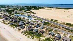 An aerial view of a coastal residential area with houses, a beach, and a road.