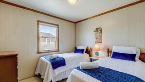 A room with two beds, a wooden dresser, a window, and a wall-mounted lamp.