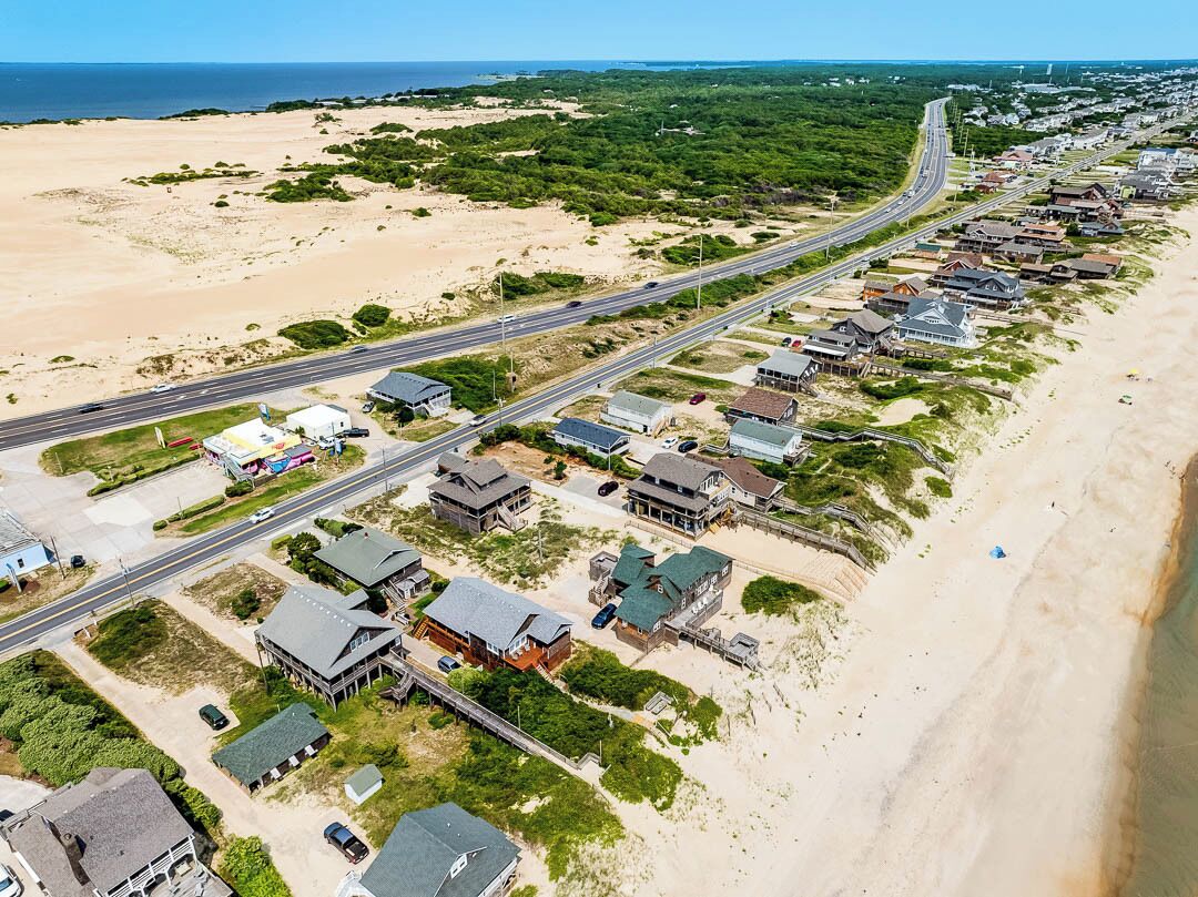Vue aérienne d’une zone résidentielle côtière, avec des maisons le long de la plage, une route principale et une autoroute.