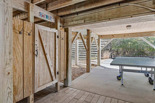 Una estructura de madera con una mesa de ping pong, un letrero que dice 'Beach Bum' y un área techada con vista a árboles.