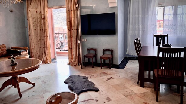 A living room with a TV, a dining table, chairs, a chandelier, and a view of the outside. - Comfortable apartment in the center of Gueliz, close to all amenities. (Marrakech)