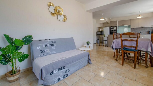A modern living room with a sofa, a dining table, chairs, a kitchen in the background, and a potted plant. - La Maison d'à côté - CRANCEY (CRANCEY)