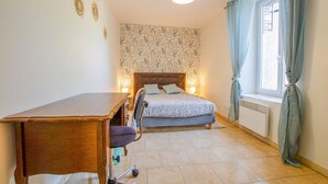 A bedroom with a bed, a desk, a chair, a window with curtains, and a patterned wall. - La Maison d'à côté - CRANCEY (CRANCEY)