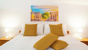 Une chambre d’hôtel avec un lit, deux tables de chevet et un tableau représentant des ruines antiques accroché au mur.