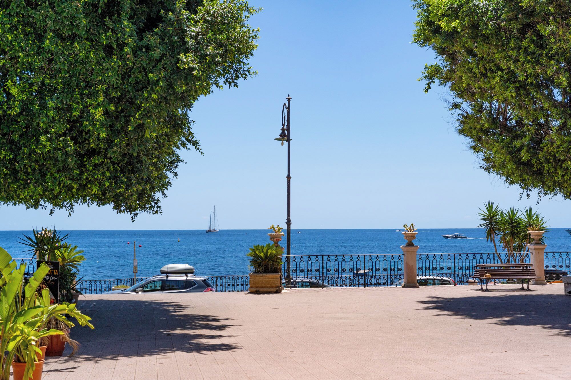 A coastal promenade with a clear view of the sea, a bench, and a street lamp.