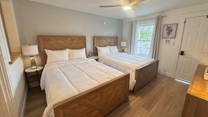A bedroom with two beds, a ceiling fan, a nightstand, a lamp, and a door with a window view. - Walk to Beach & Pier | 1BR Suite with Pool & Kitchenette (Old Orchard Beach)