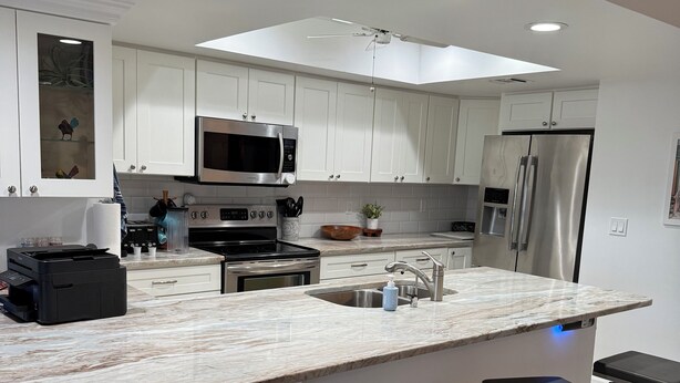 A modern kitchen with white cabinets, stainless steel appliances, a marble countertop, and bar stools. - Charming 3-bedroom townhome with a river view and a 40 boat slip in Fort Pierce (Fort Pierce)
