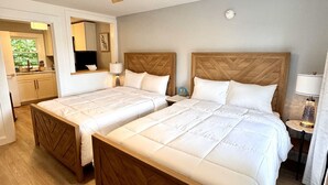 Ein Hotelzimmer mit zwei Betten, einem Deckenventilator, einem kleinen Tisch mit Lampe und Blick ins Freie.