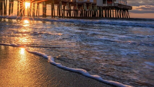 A beachfront property with a pier extending into the ocean, featuring multiple levels with balconies and a restaurant.