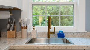 A kitchen with a stainless steel sink, a gold faucet, and a window with a view of greenery.