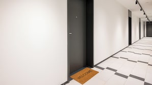 Un couloir d’hôtel moderne avec un paillasson, une porte portant une pancarte et un sol carrelé.