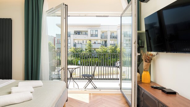 Une chambre d’hôtel comprenant un lit, une télévision, une petite table avec une chaise et un balcon donnant sur l’extérieur.