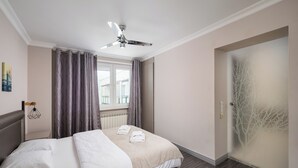 A hotel room with a bed, a ceiling fan, a window with curtains, and a wall with a tree design.
