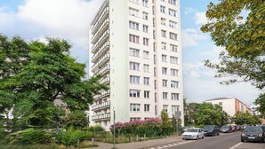 A multi-story residential building with balconies, surrounded by greenery and parked cars.