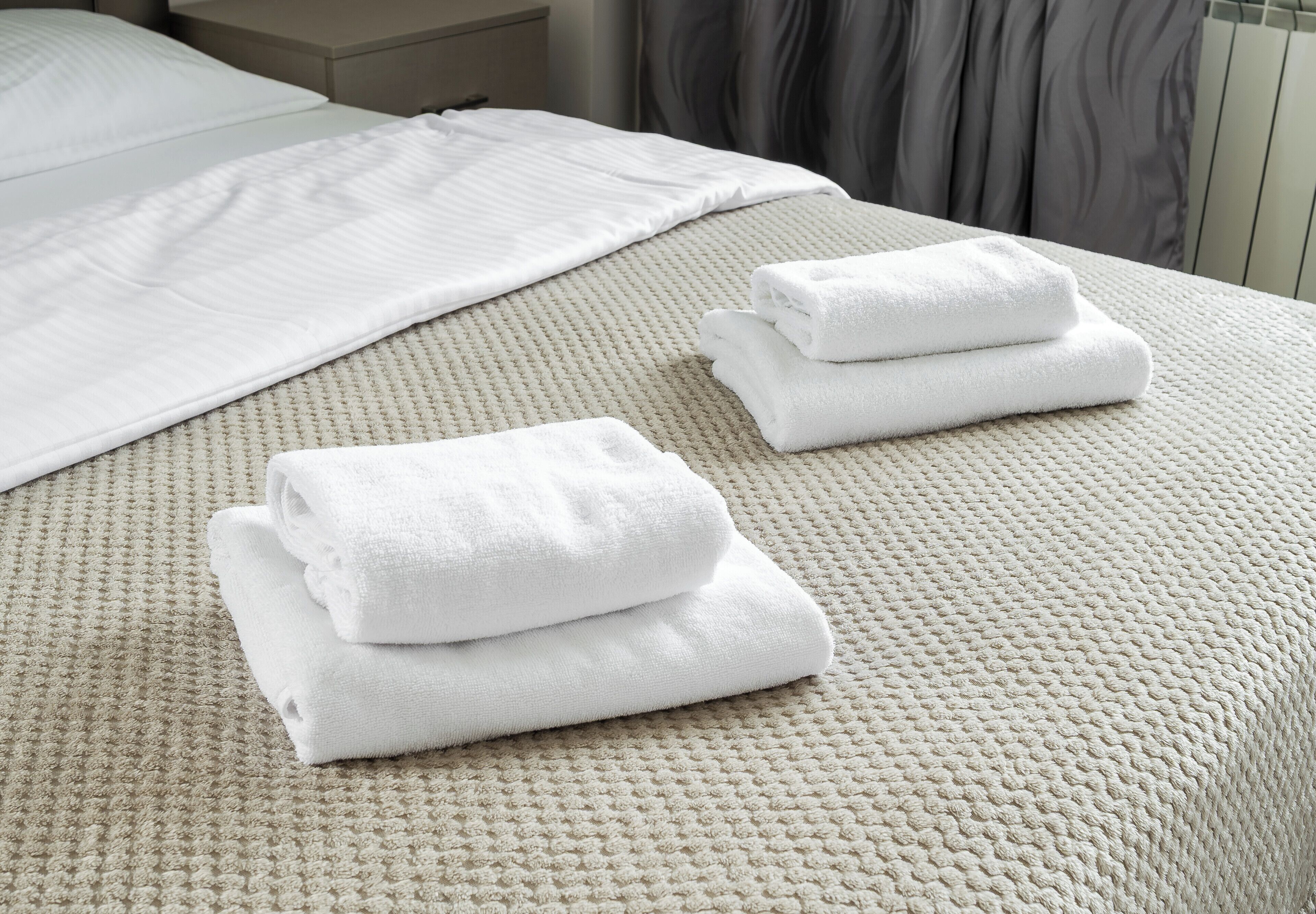 A neatly made bed with a textured beige bedspread and two folded white towels on the bed.
