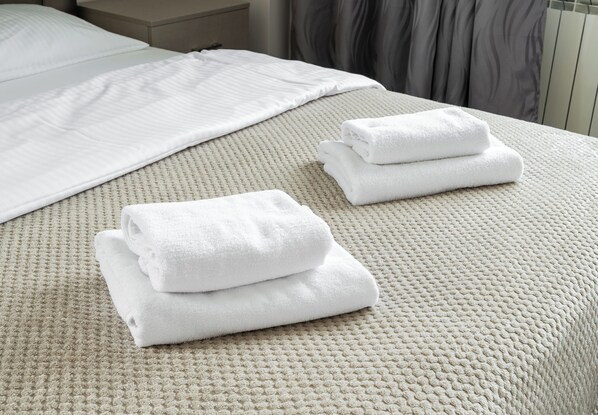 A neatly made bed with a textured beige bedspread and two folded white towels on the bed.
