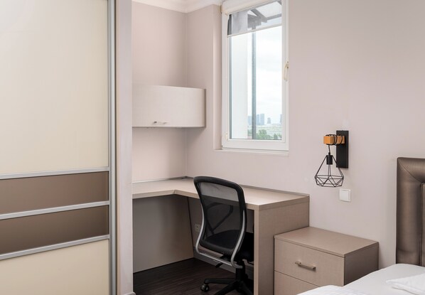 A bedroom with a desk, a chair, a bed, a nightstand, and a window with a view of the city.