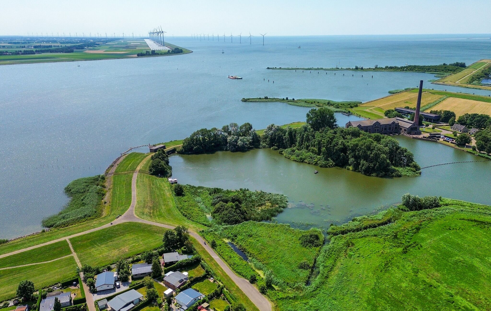 Luchtbeeld van een kustgebied met windturbines, een meer en woongebouwen.