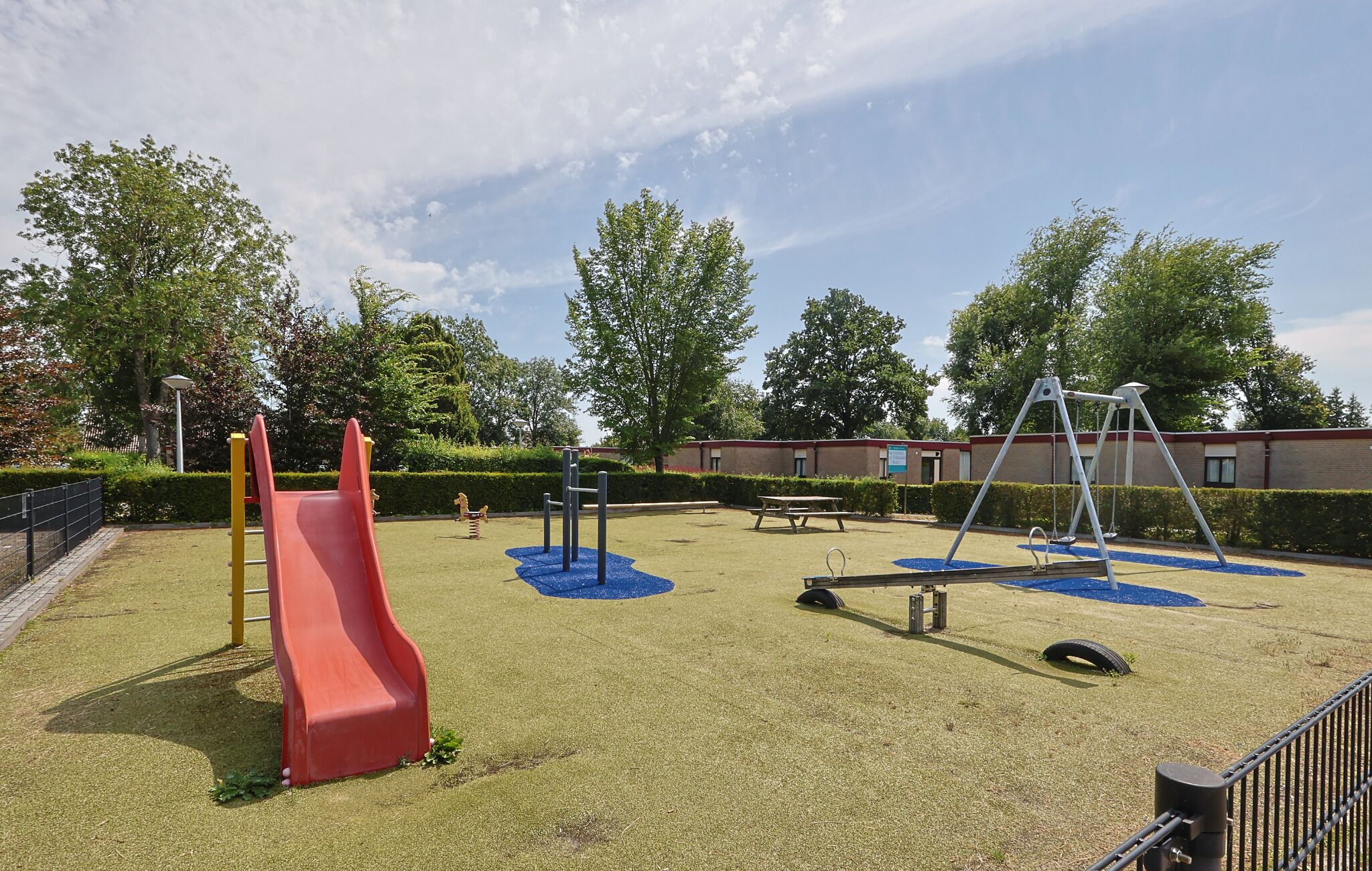 A playground with a red slide, swings, and a blue play area.
