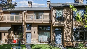 A two-story building with a stone facade, multiple windows, and a front porch with outdoor seating. - Cedars 3: Ski-In/Out Peak 9 Townhome, Fireplace, Pool & Hot Tub Access. (Breckenridge)