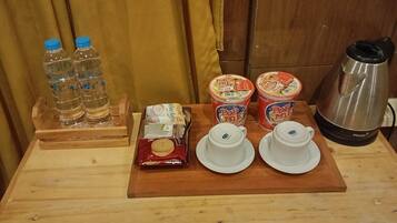 A wooden table with a tray containing water bottles, a pack of biscuits, two containers of PopMe tea, and a coffee maker.