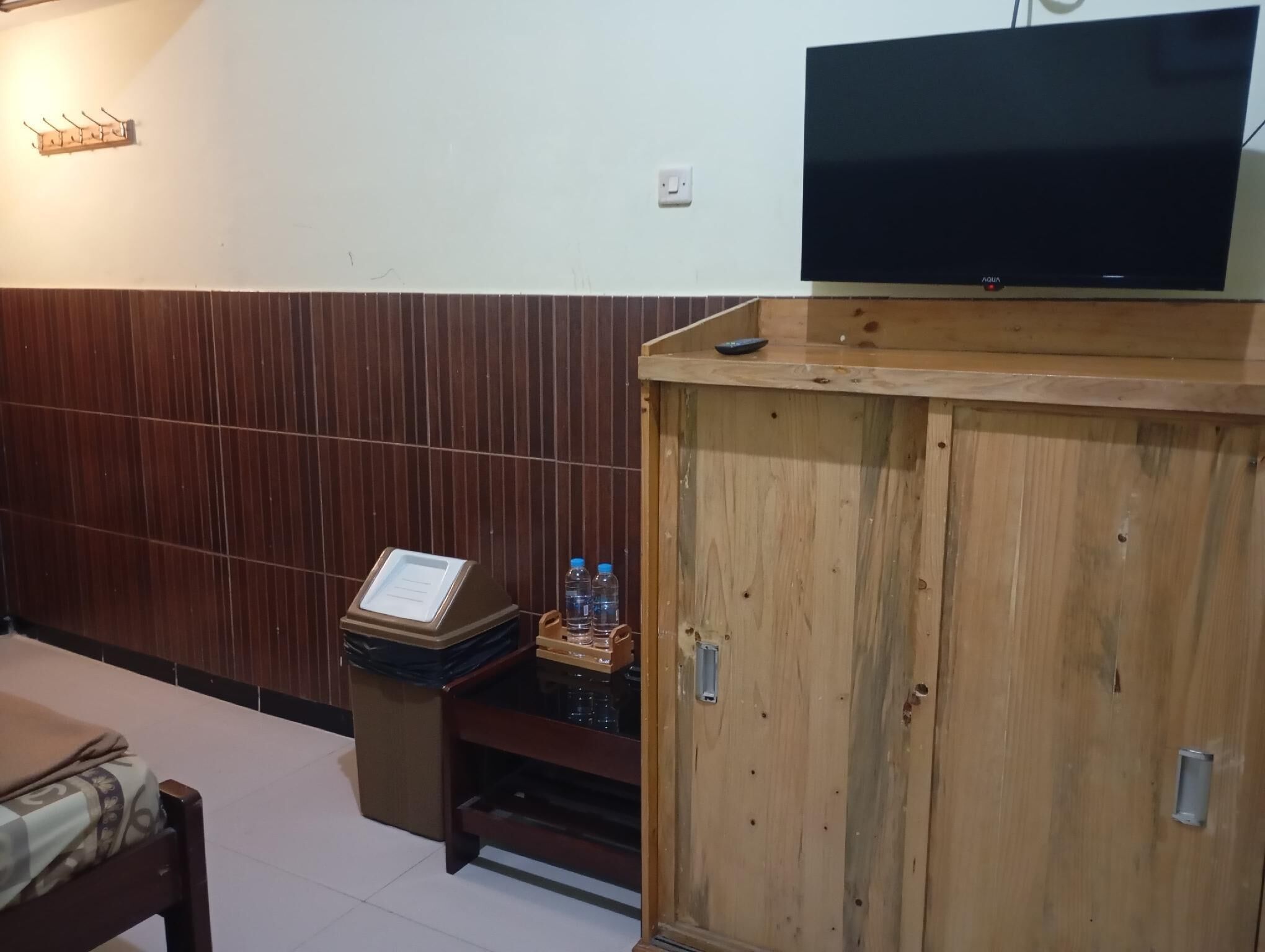 A hotel room with a wooden cabinet, a television on top, a small table with water bottles, and a bed with a patterned bedspread.