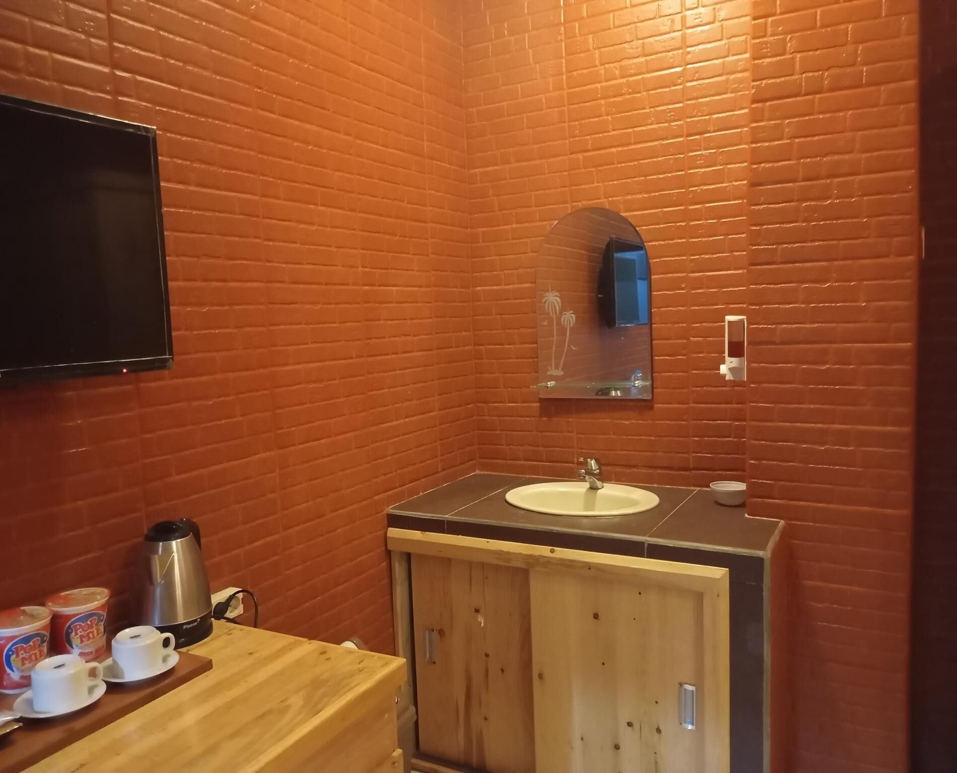 Un baño con tocador de madera, lavabo, espejo y televisor montado en la pared.