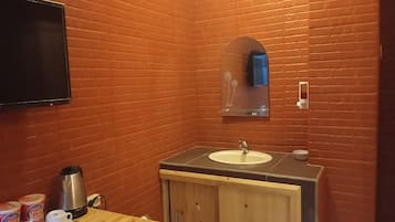 Un baño con tocador de madera, lavabo, espejo y televisor montado en la pared.