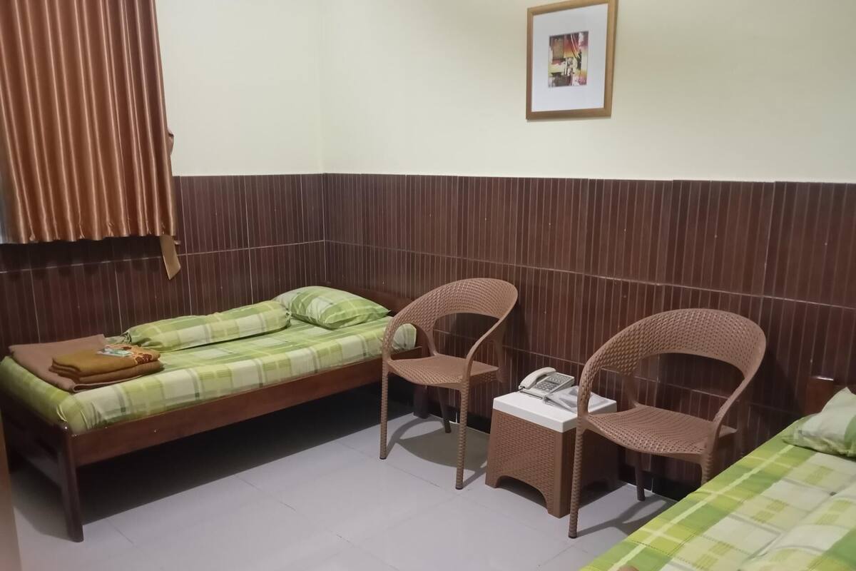 Una habitación con dos camas, una silla, una mesita con teléfono y un cuadro en la pared.