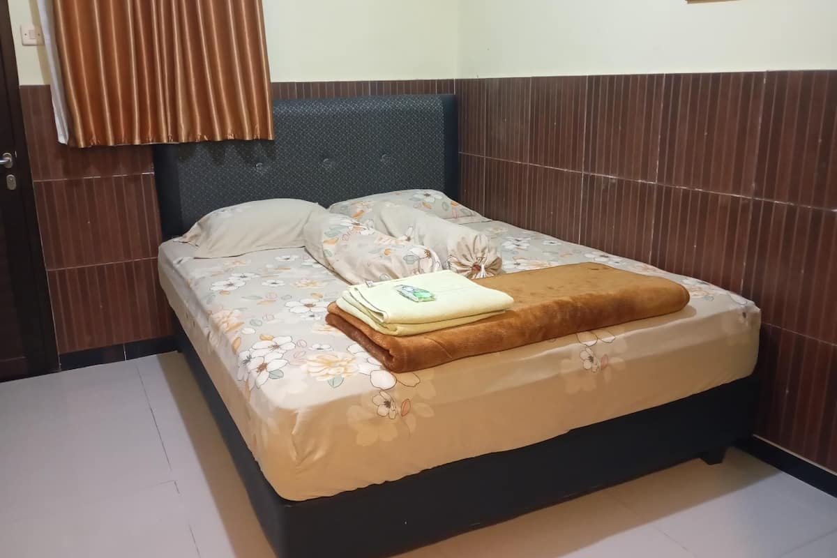 Una cama bien hecha con ropa de cama floral, una manta marrón y una toalla doblada.