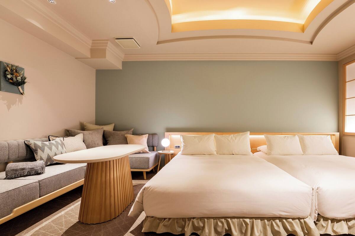 A hotel room with a large bed, a sofa, a small table, and a wall-mounted clock.