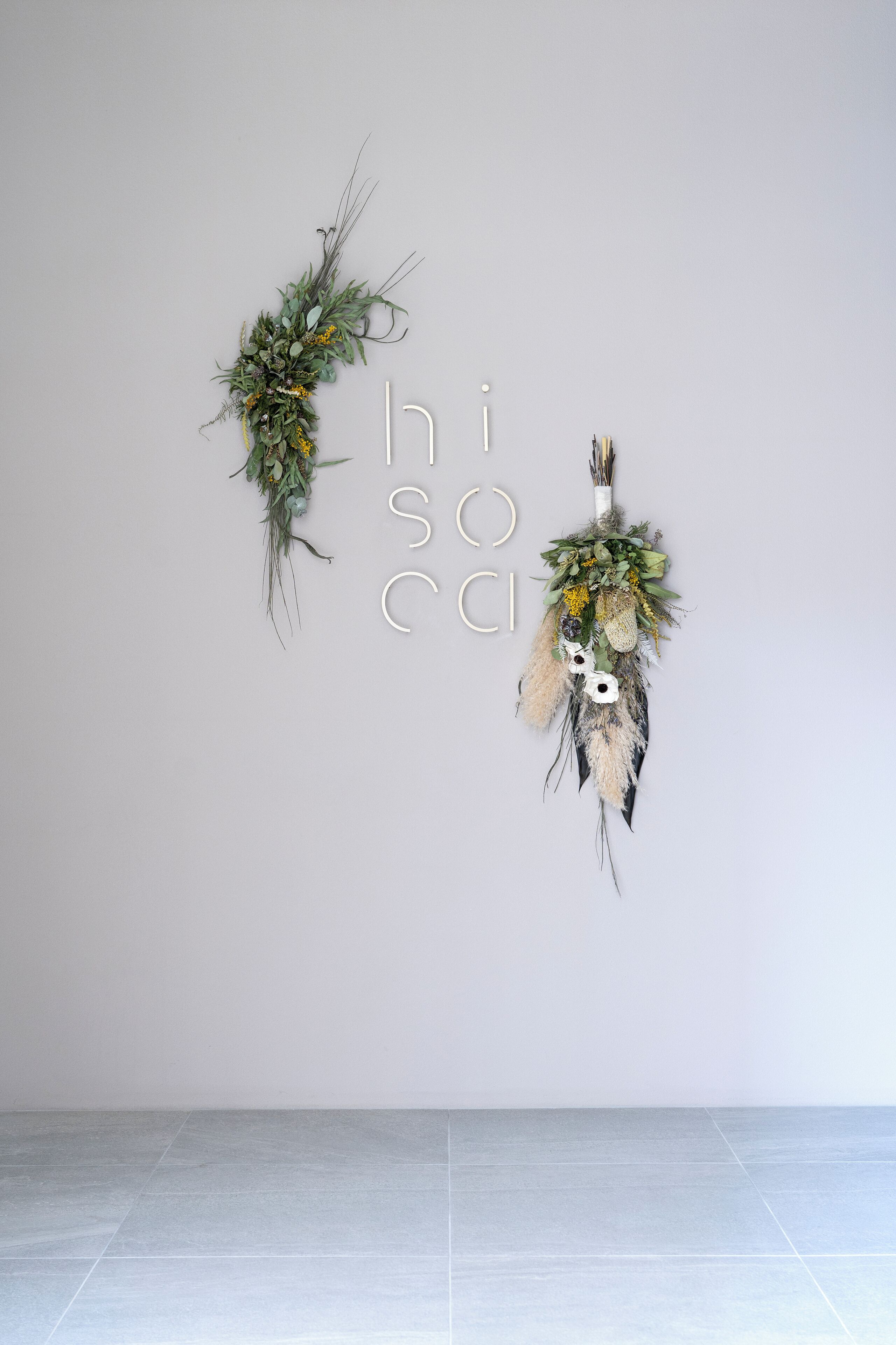 Two wall-mounted floral arrangements against a plain wall.
