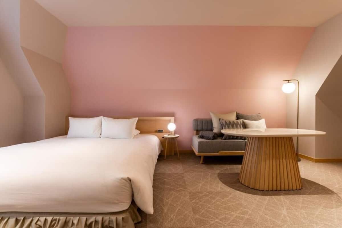 A hotel room with a large bed, a small sofa, a round table, and a lamp.