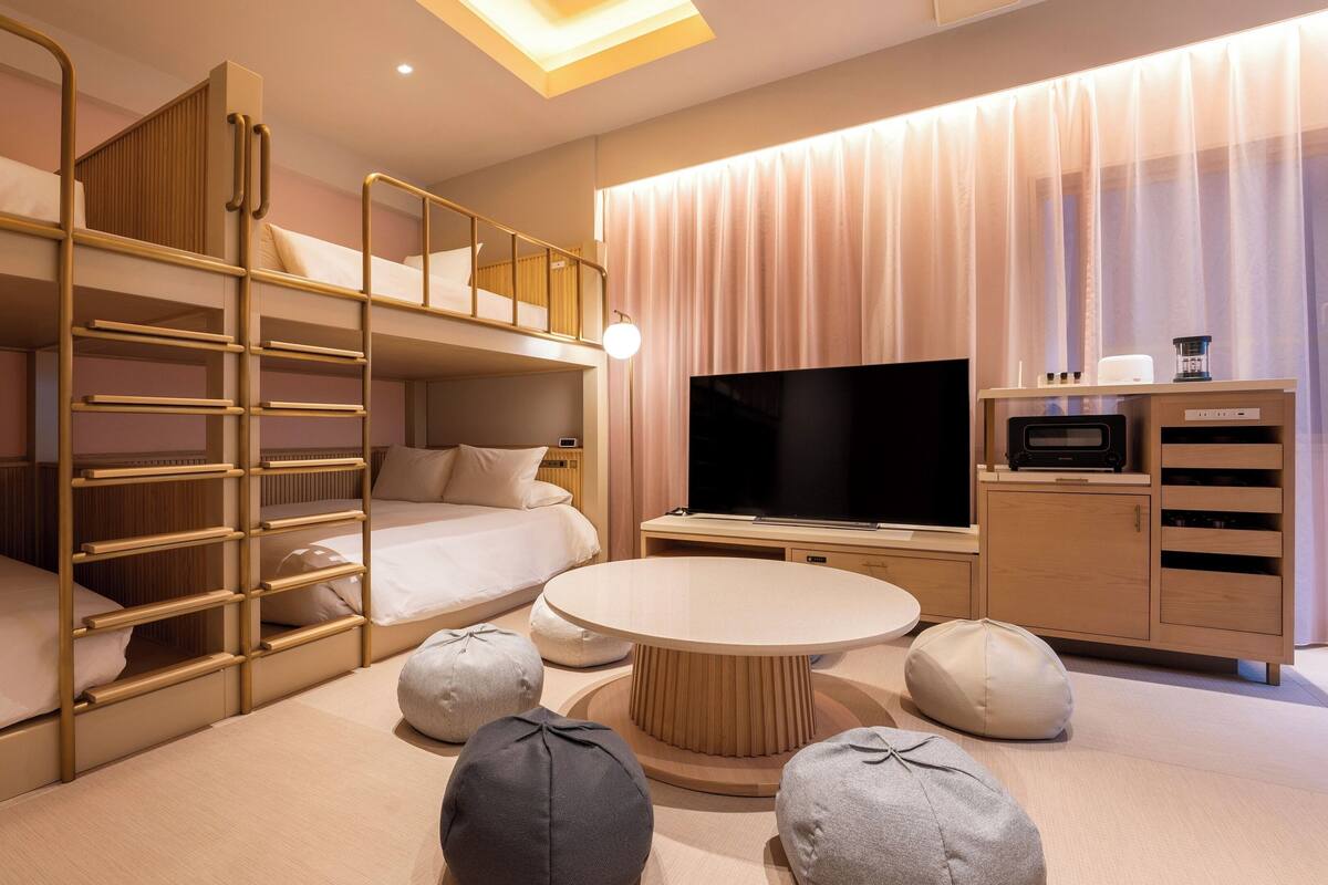 A hotel room with bunk beds, a TV, a round coffee table, and ottomans.